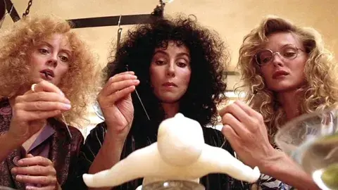 The three witches, Susan Sarandon, Cher, and Michelle Pfeiffer are pocking a voodoo doll with needless