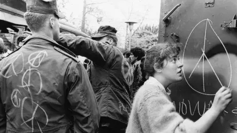 solder looking at a man drawing a peace sign on a poster